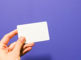a hand holding a white business card against a purple background